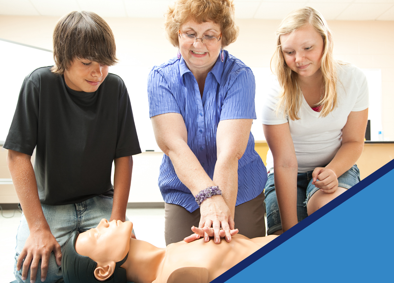 Courses Instructor teaching two younger students in one of our CPR courses. The instructors has their hands pressed on a CPR mannequin's chest.
